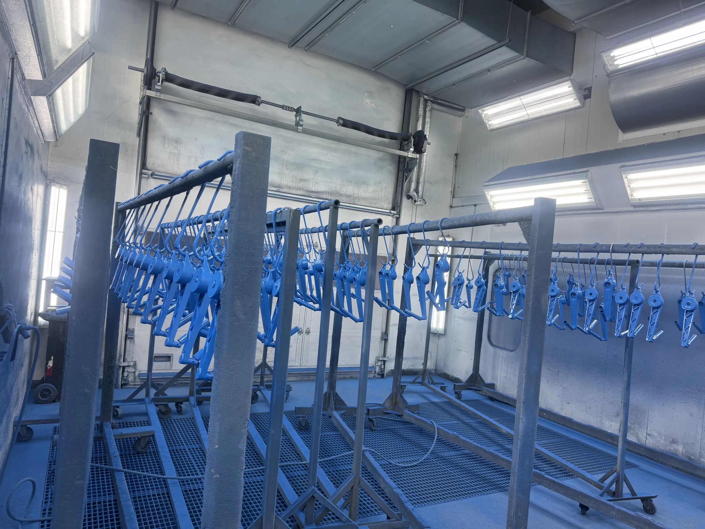 Blaue Metallteile hängen zum Trocknen in der Spritzkabine – Industrielackierung Augsburg